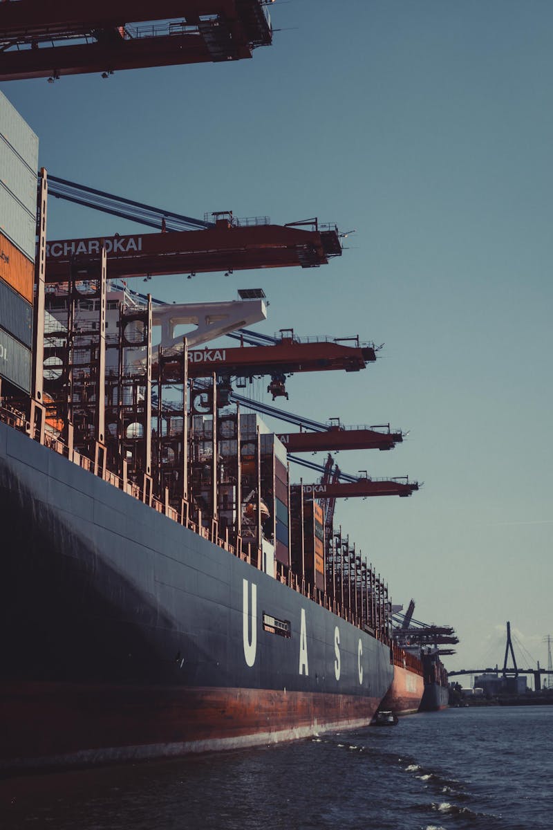 A large cargo ship docked at Hamburg Harbor, cranes loading containers under a clear sky.